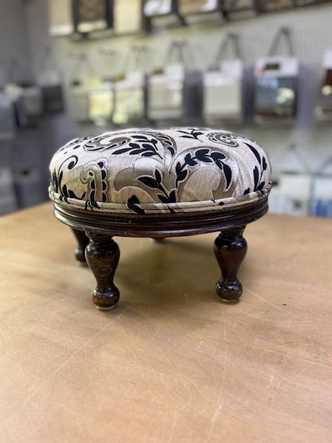 A dark wooden chair with a carved back and a blue upholstered seat stands in front of a gray, textured wall.
