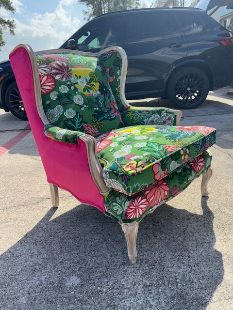 Brightly upholstered wingback chair outdoors, pink back, floral seat, light wood frame, car background.