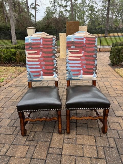 Two wooden dining chairs with dark leather seats and patterned backs on a brick patio.