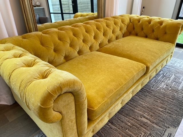 Yellow tufted sofa with rolled arms, in a well-lit room with a gold mirror.