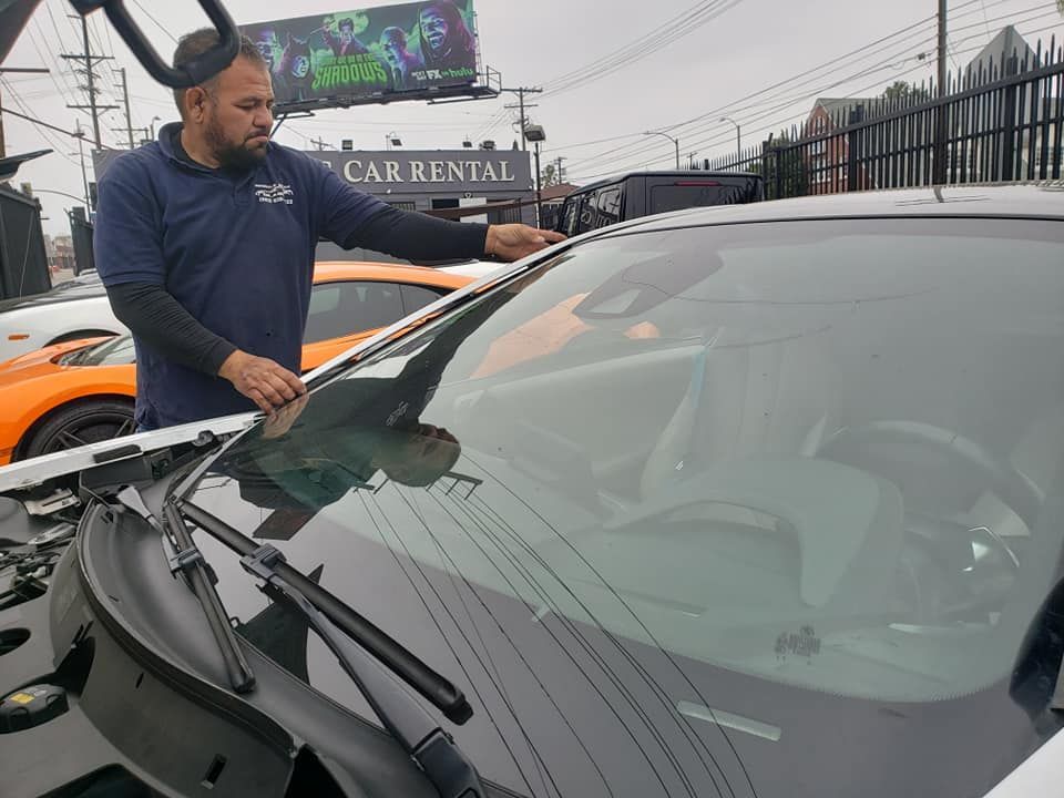 Man inspecting the windshield of a white car outside a car rental business.
