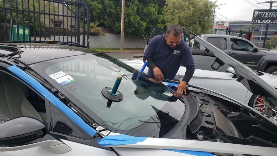 Man repairing a car windshield outdoors, using tools and suction cup, with blue tape.