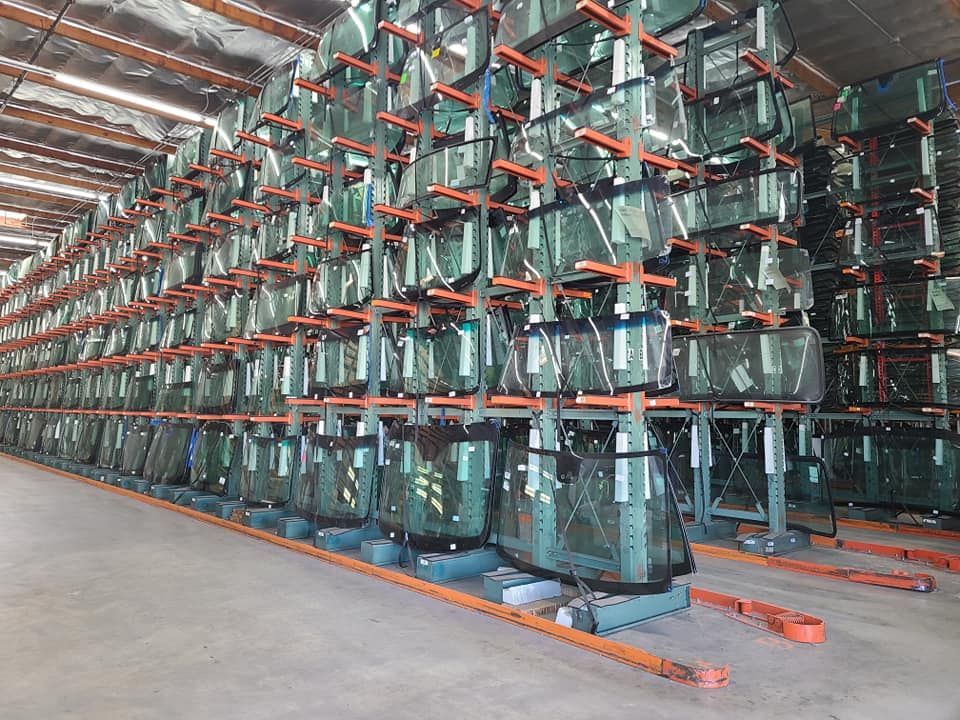 Rows of automotive glass windshields stored on metal racks in a warehouse.
