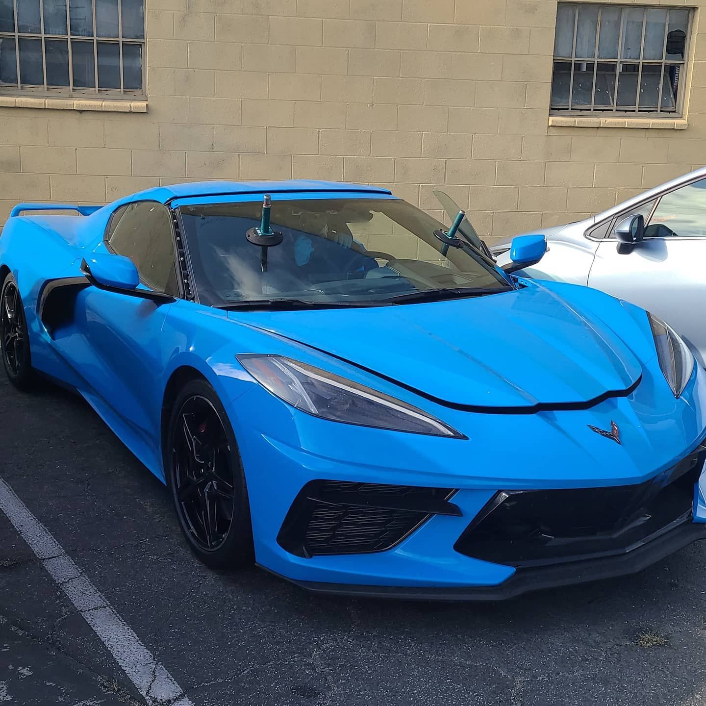 Blue Chevrolet Corvette sports car parked next to a silver car in front of a brick building.