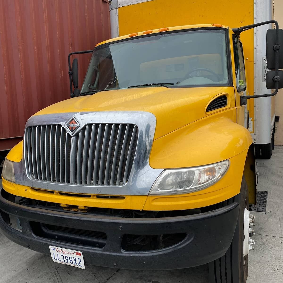 Yellow International box truck with a silver grill parked outdoors.
