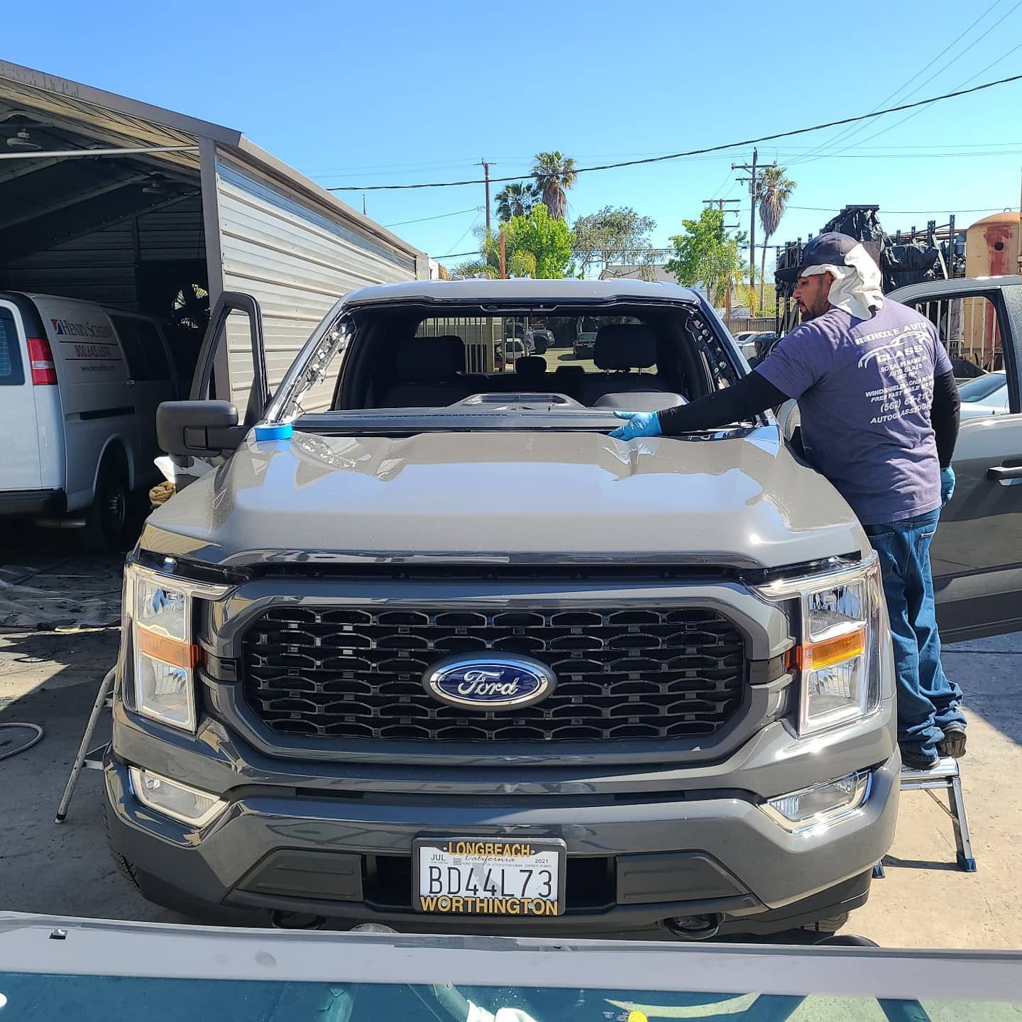 A technician replaces a windshield on a gray Ford truck outdoors.