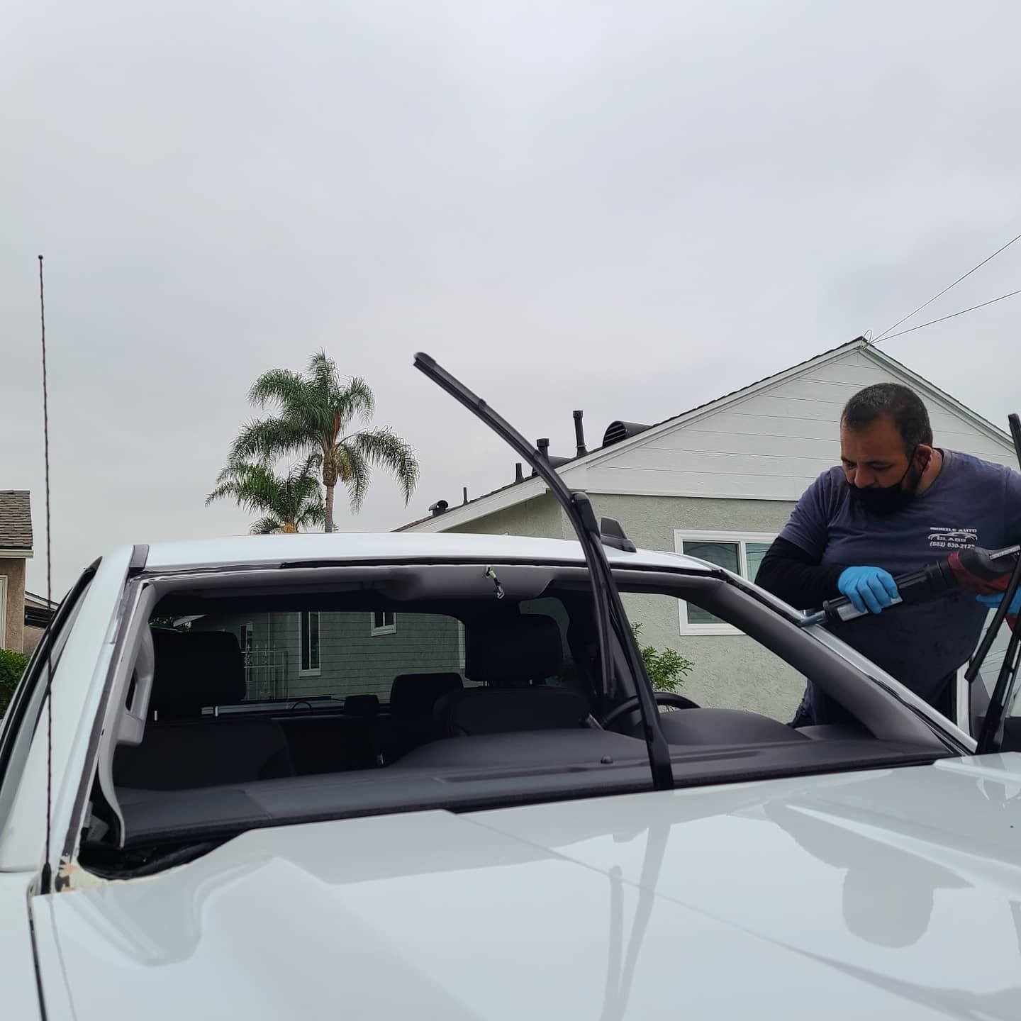 A person replacing a windshield on a white truck outdoors on a cloudy day.