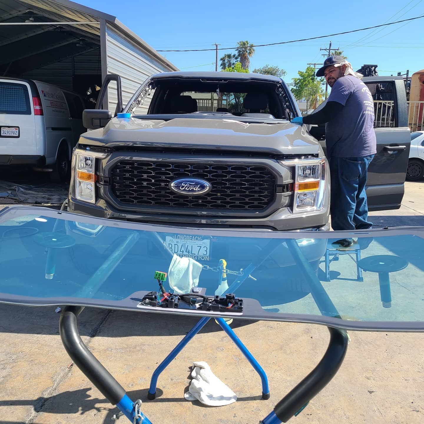 Truck windshield replacement: A man works on a gray Ford truck; a new windshield sits in a blue support.