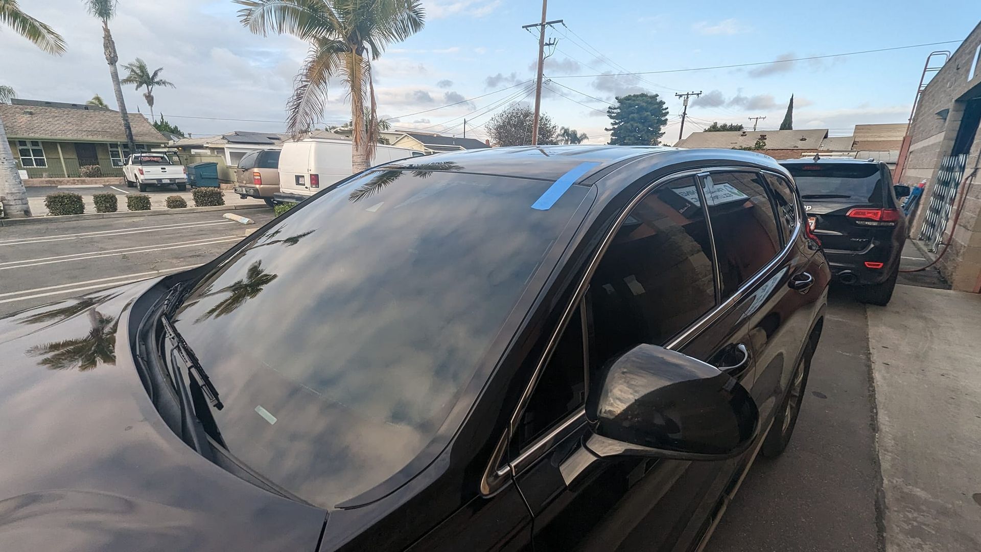 Black car parked outdoors, reflecting sky and surrounding buildings.