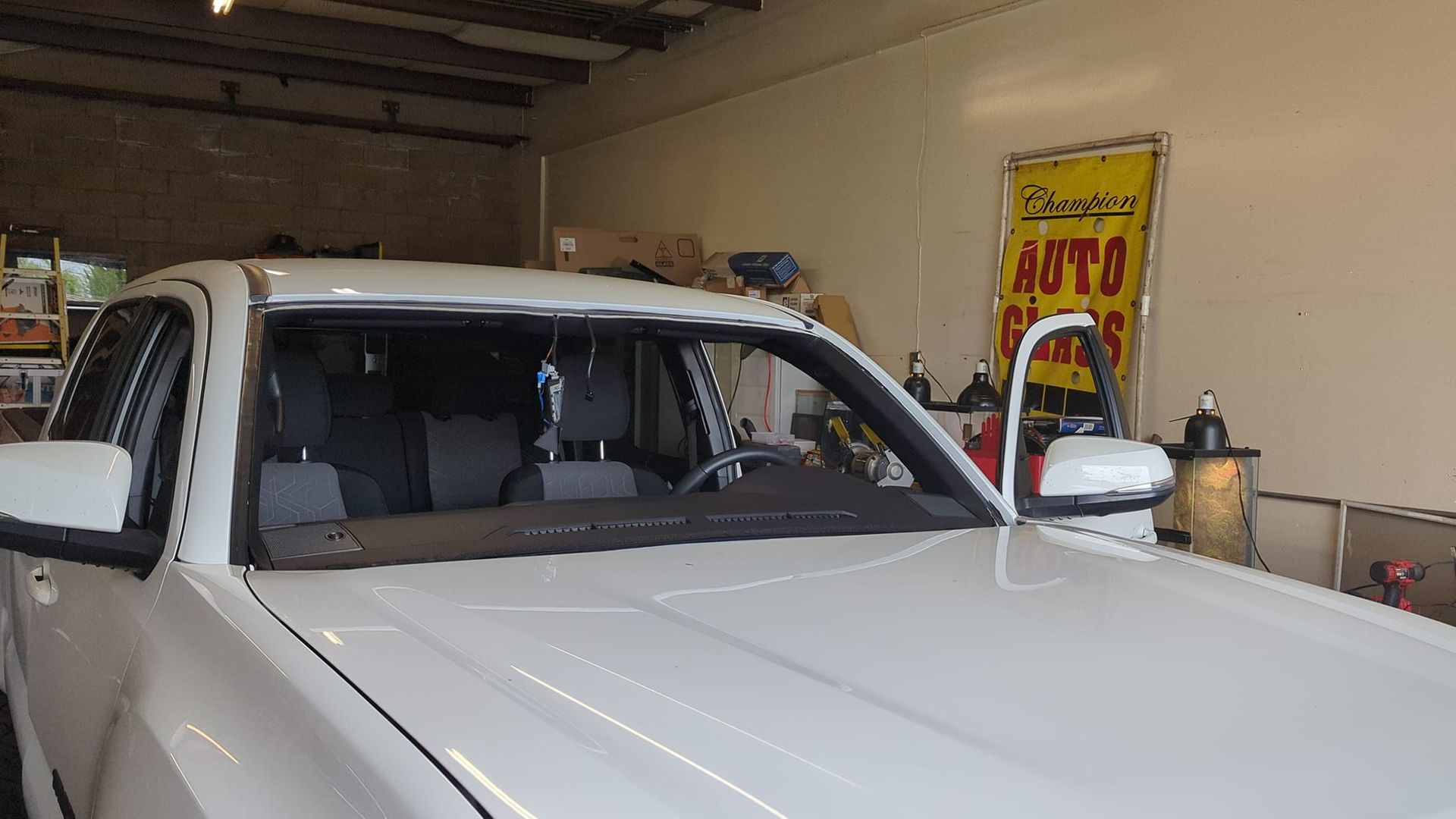 White pickup truck inside an auto repair shop with the windshield removed, door open.