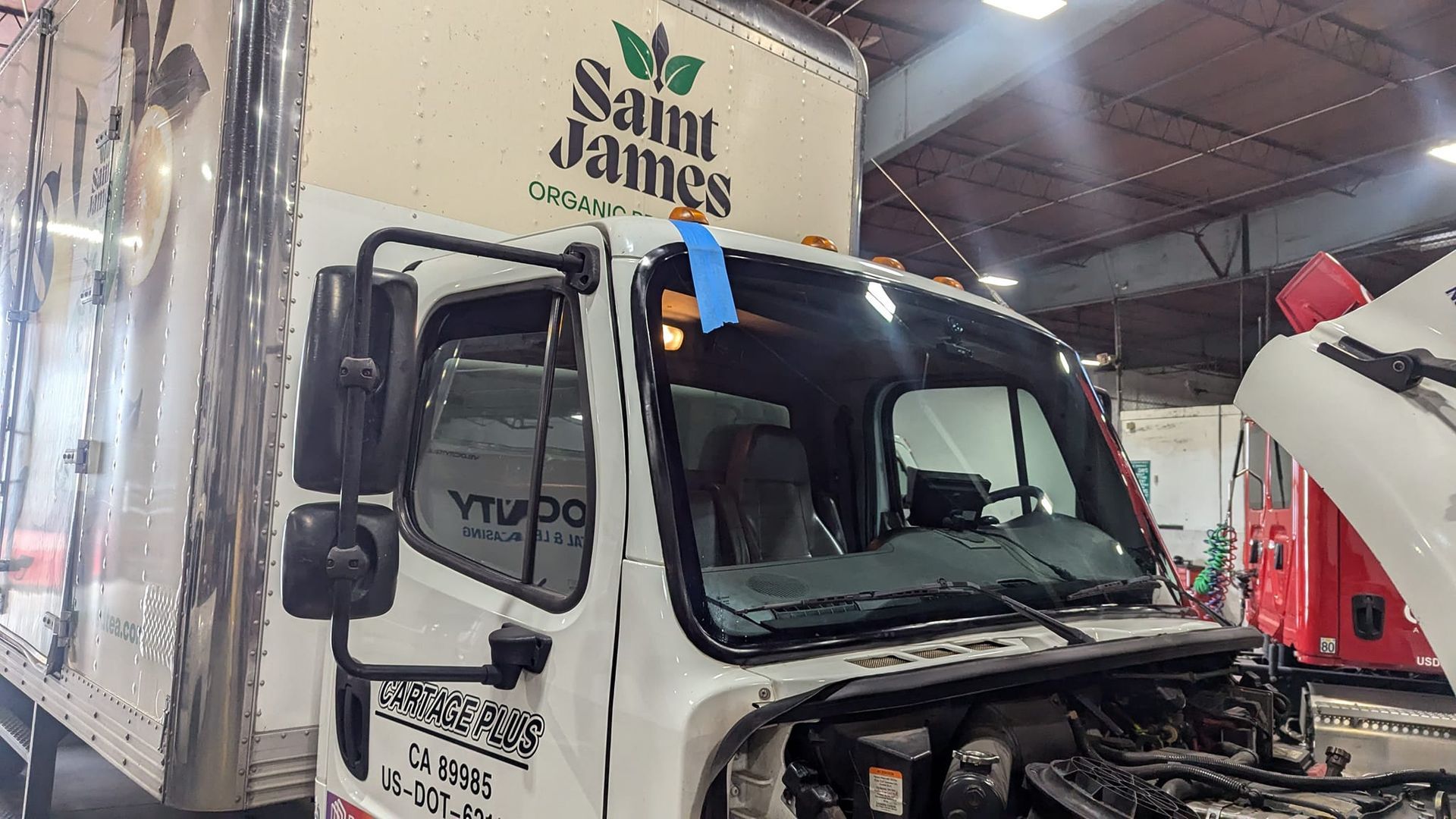 White delivery truck in a repair shop. The hood is open, and a Saint James logo is visible.