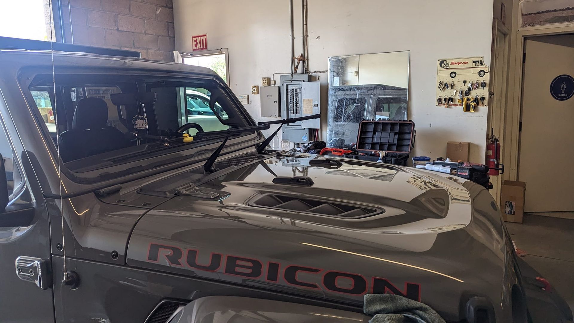 Gray Jeep Rubicon hood in a garage, with interior visible and tools in the background.
