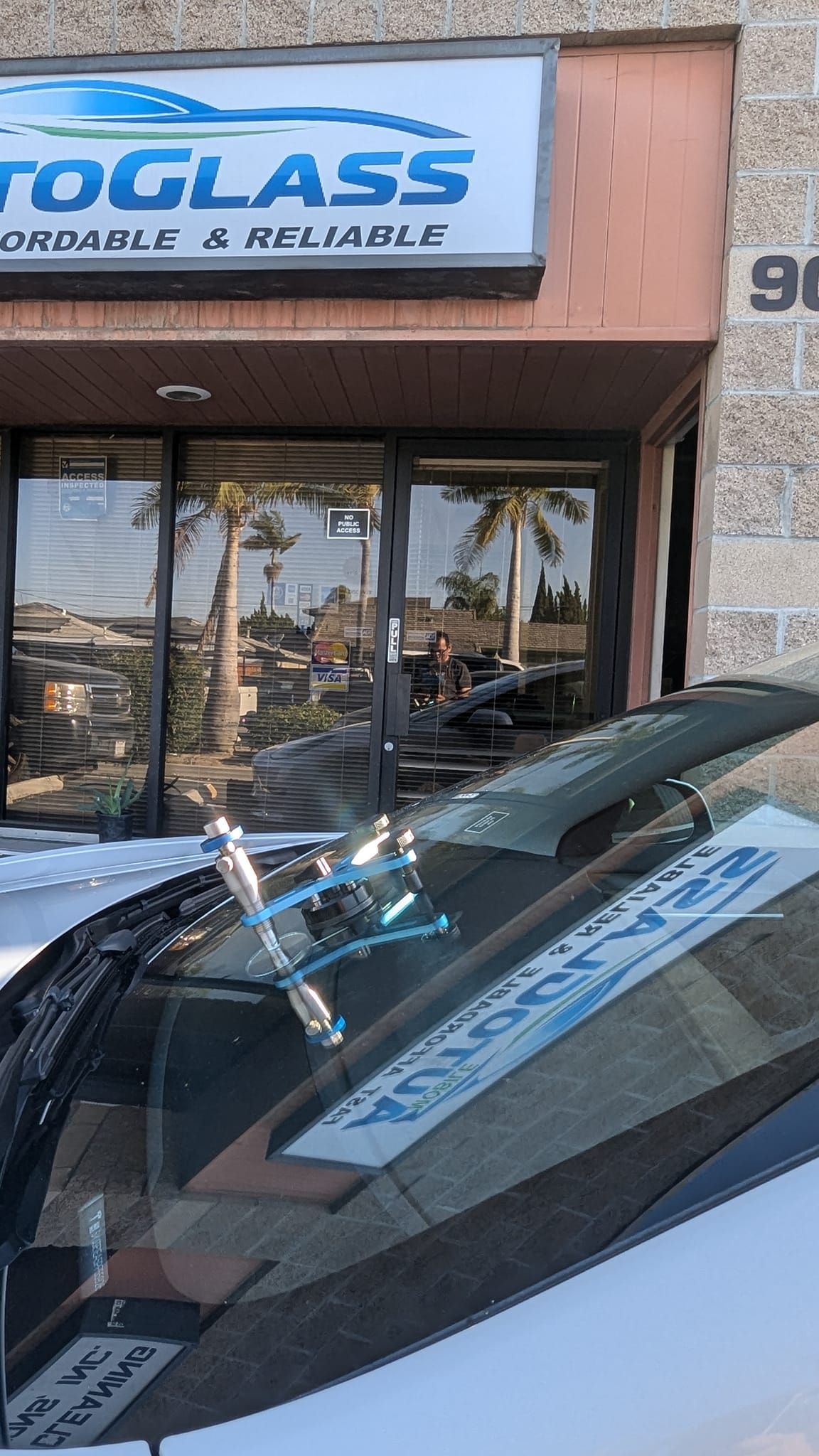 Windshield repair service with tool on a car in front of a glass shop.