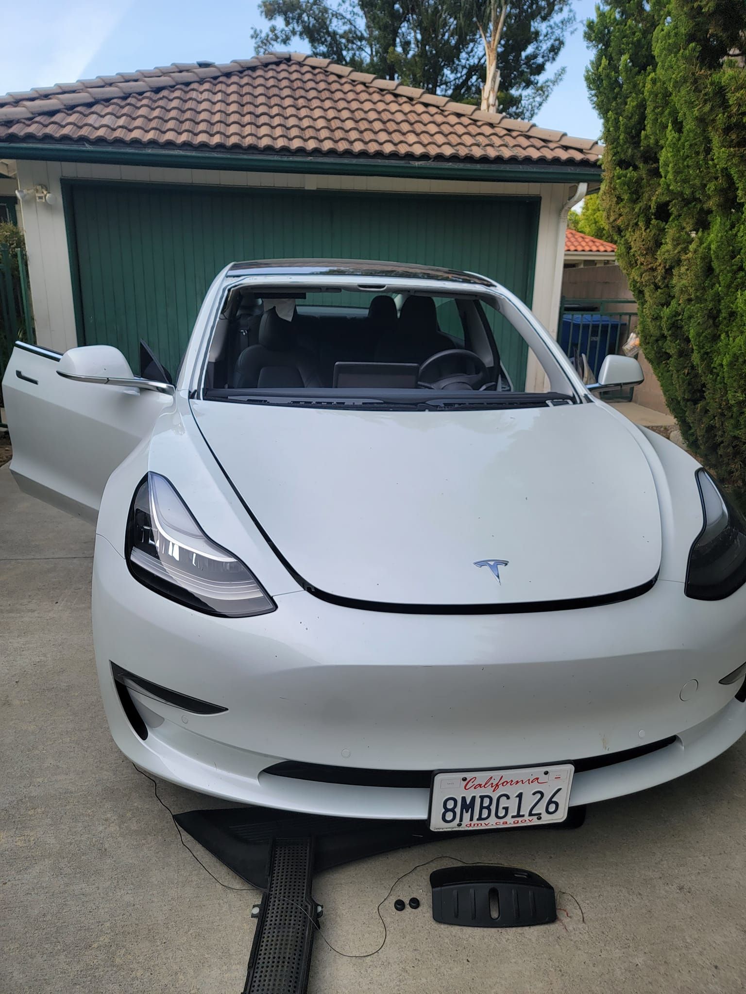 White Tesla Model 3 with open doors in front of a green garage.