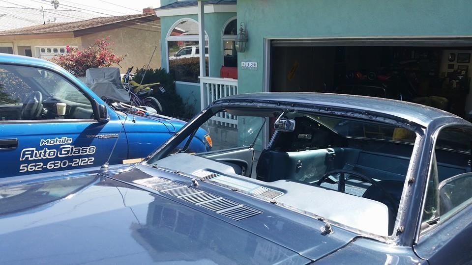 Blue classic car being worked on in front of a turquoise house, with a blue truck parked beside it.