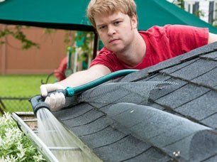 A man cleaning gutters with a water hose