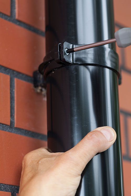 A person is installing a gutter drainage with a screwdriver on a brick wall