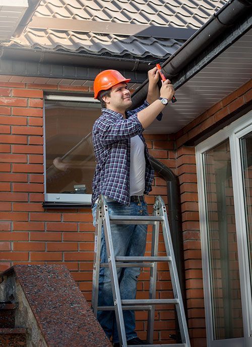 A man is standing on a ladder fixing a gutter