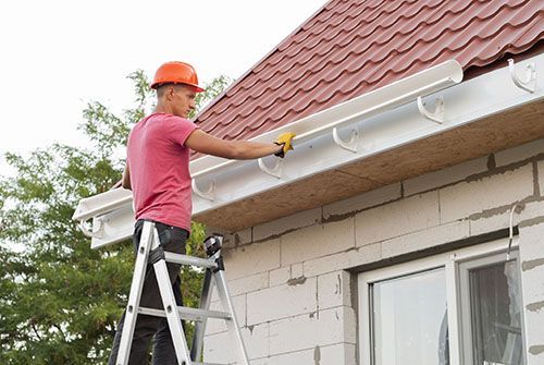 A man is standing on a ladder fixing a gutter on a roof