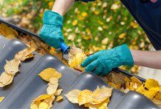 A person is cleaning a gutter with a broom and leaves.