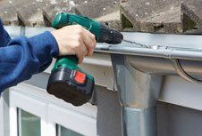 A person is using a cordless drill to install a gutter on a roof.