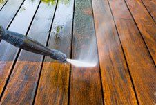 A person is using a high-pressure washer to clean a wooden deck.
