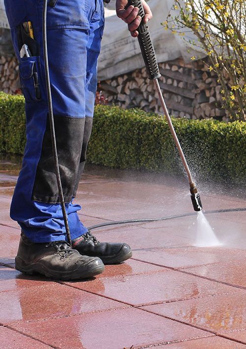 A man is using a high pressure washer to clean a patio