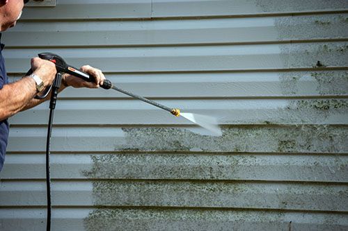 A man is cleaning the side of a house with a high pressure washer