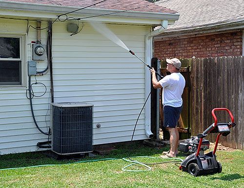 A man is using a high pressure washer to clean the side of a house