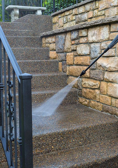 A person is using a high pressure washer to clean a set of stairs