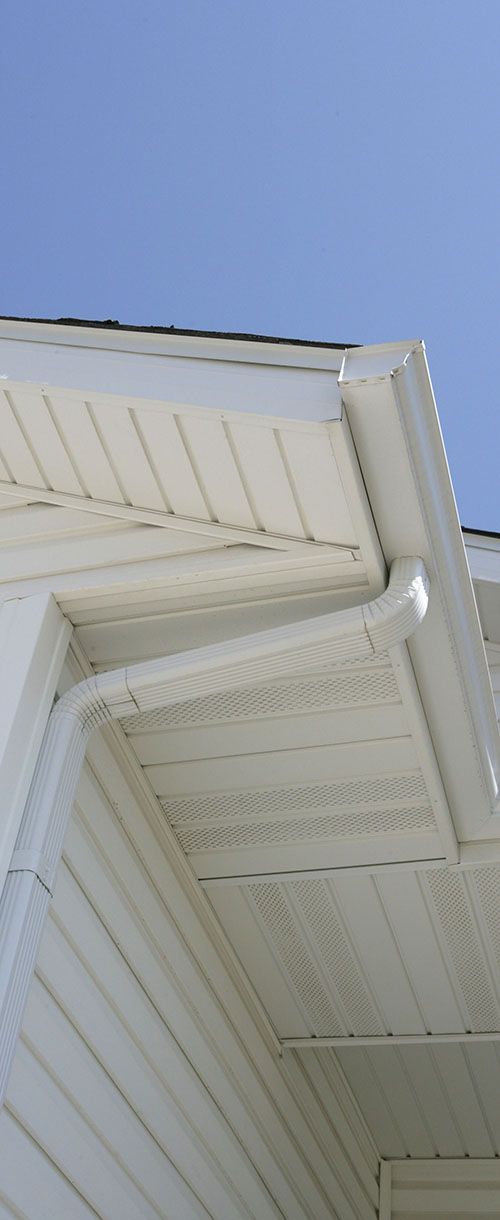 A white house with a seamless gutter on the roof and a blue sky in the background