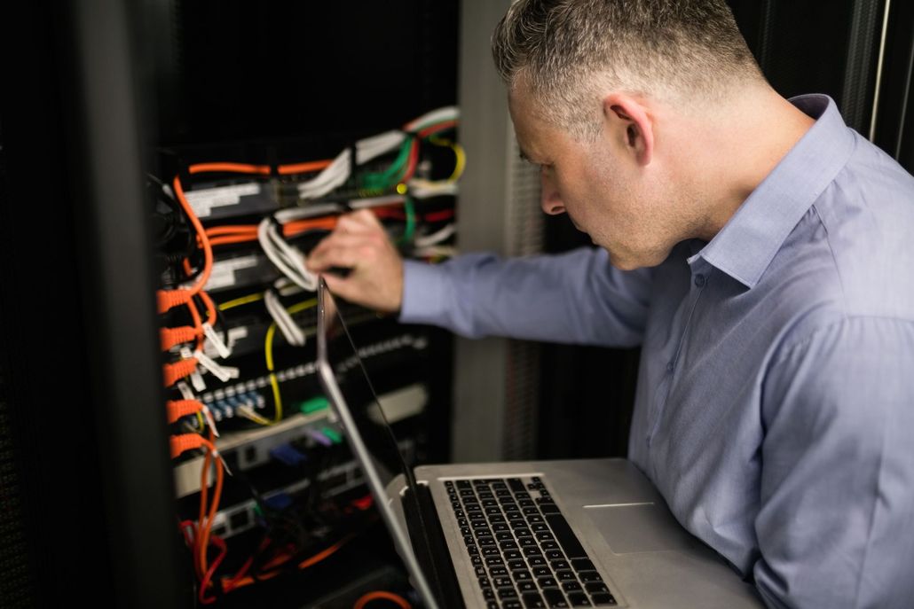 Technician inspecting network cables in a server rack beside an open laptop