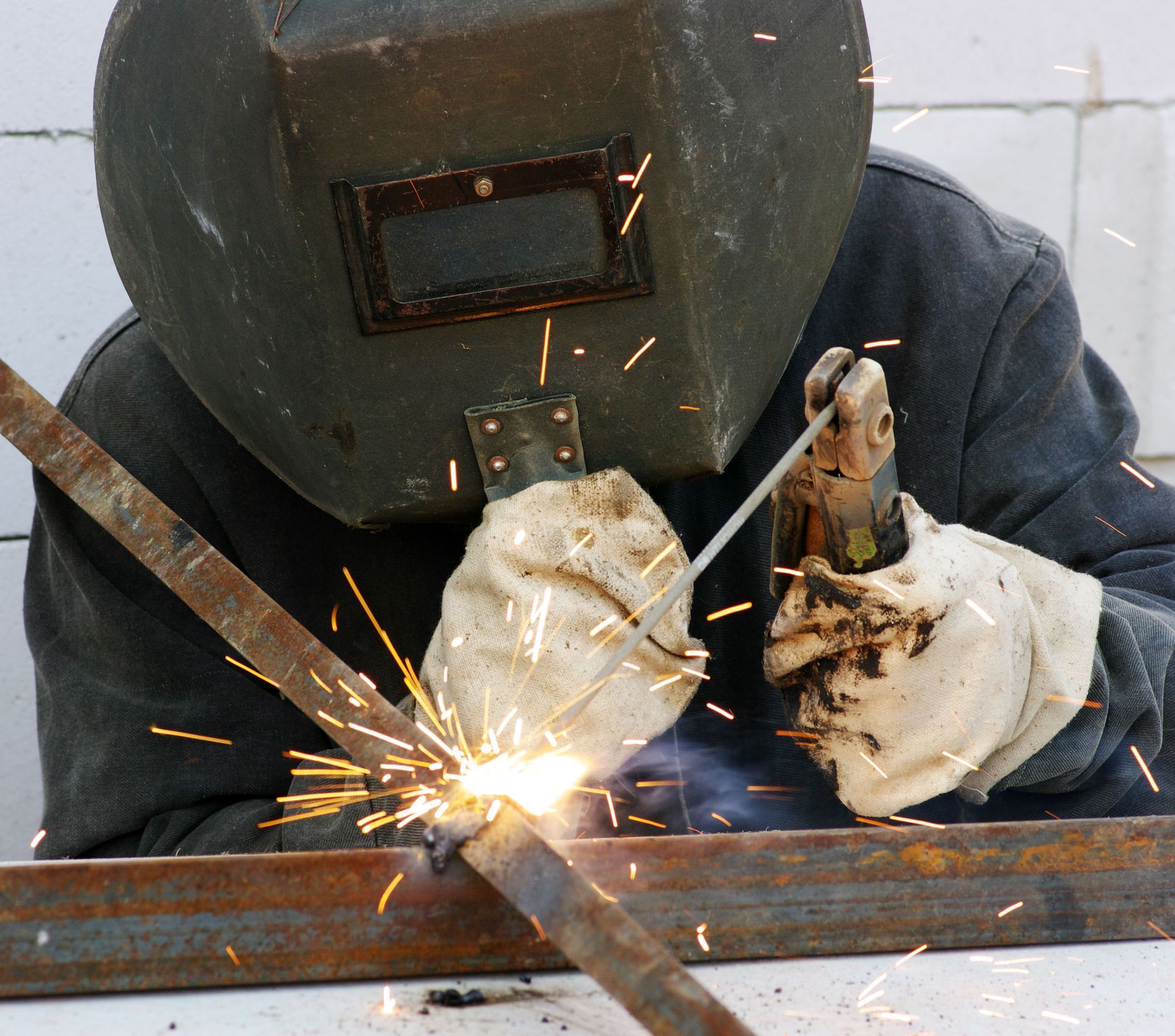 Welder in a protective mask welding metal bars, sparks flying.