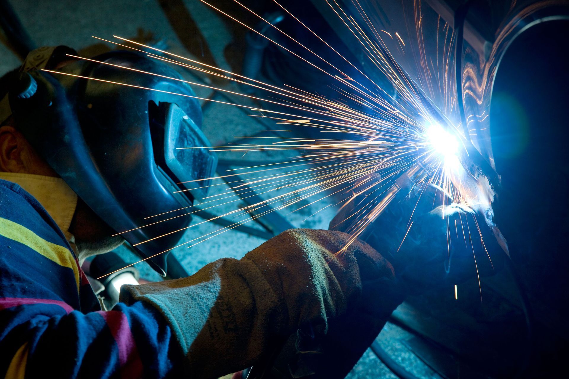 Welder wearing a protective mask and gloves, welding metal, bright sparks and blue light.