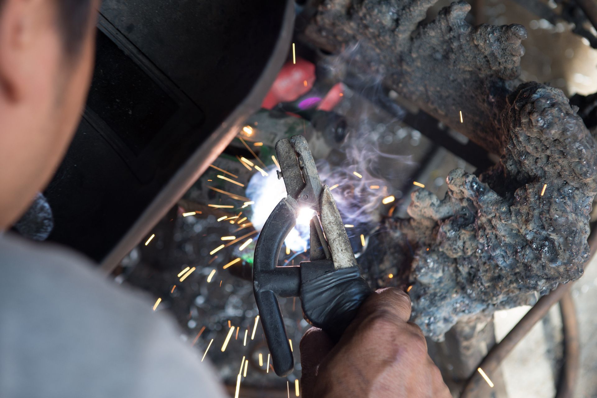 Person welding metal, sparks flying, wearing protective gear. Close-up view.