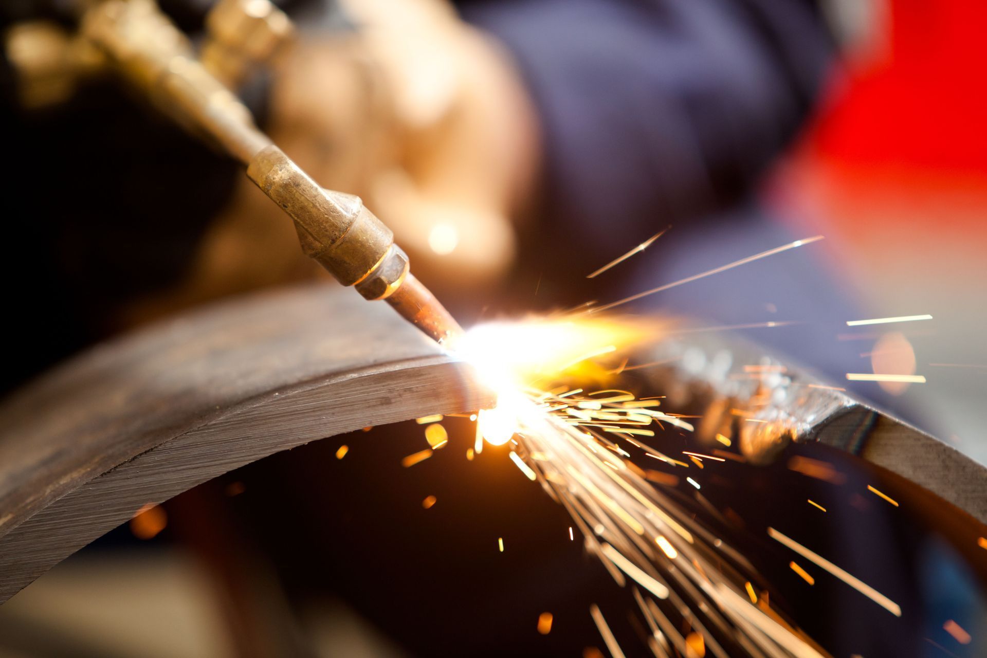 A person uses a welding torch to cut metal, bright sparks and flame visible.