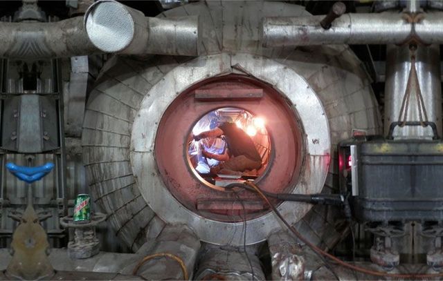 Welder working inside a large industrial machine, with bright sparks visible.