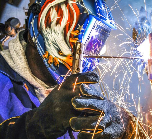 Welder wearing an eagle-decorated helmet, welding, sparks flying.