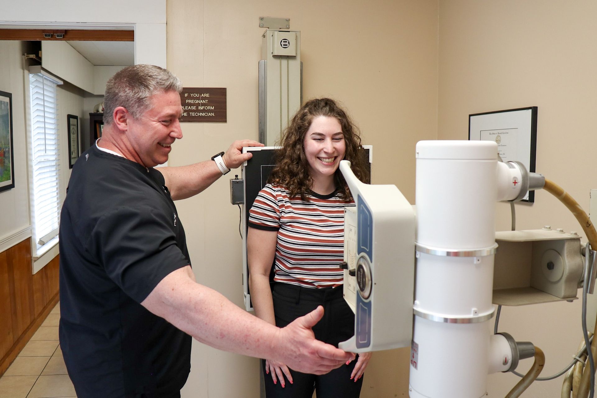 A healthcare worker assisting a young woman with an X-ray machine in a doctor's office