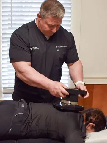 Man using a device on a person's back for treatment, likely in a clinic.