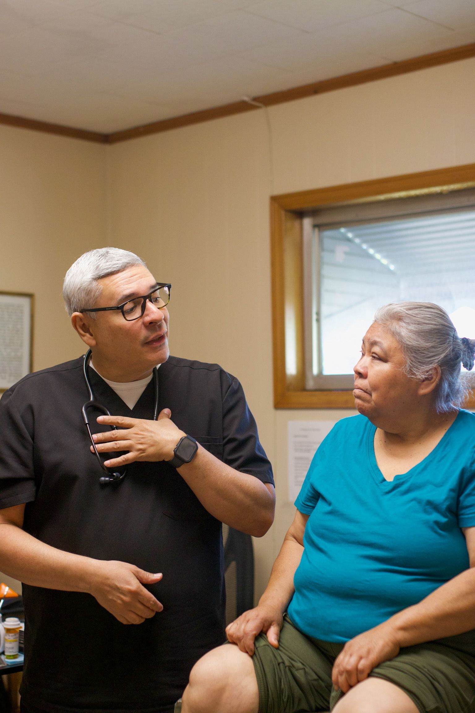 Doctor in black scrubs talking to a seated woman in a medical office