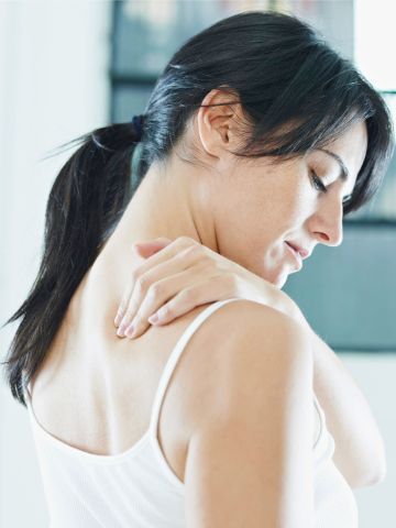 Woman in white tank top touching her shoulder, appearing to be in pain