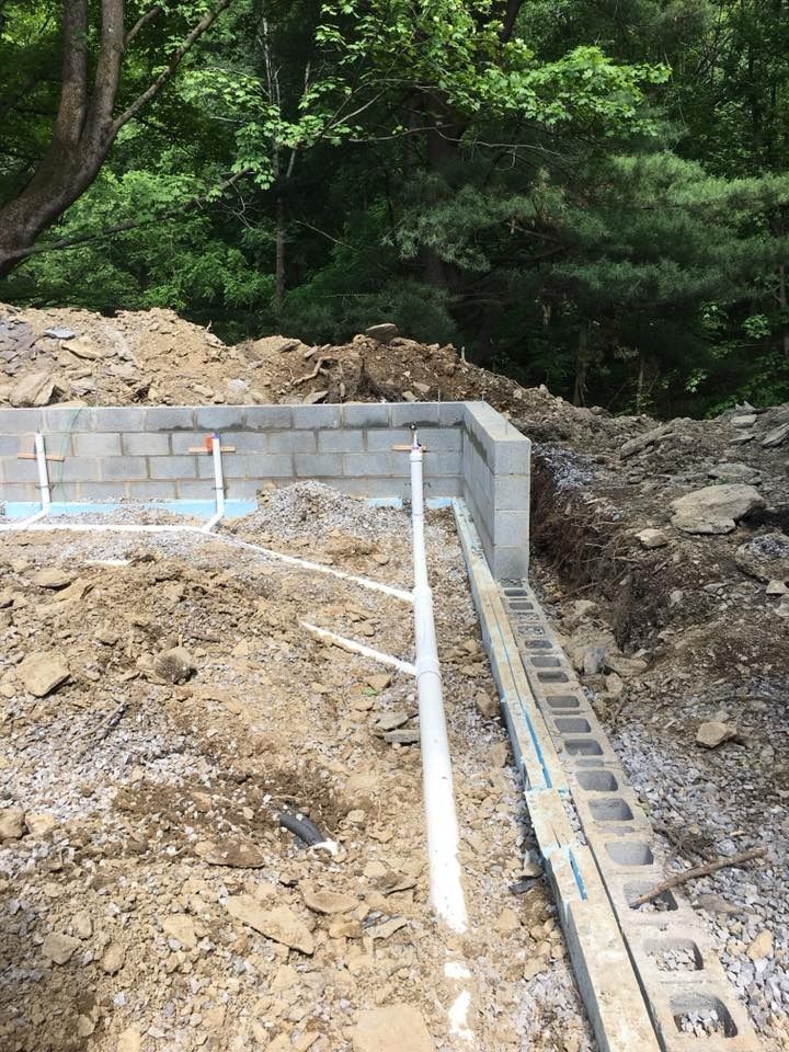 Foundation construction site with cinder block walls, pipes, and exposed earth.
