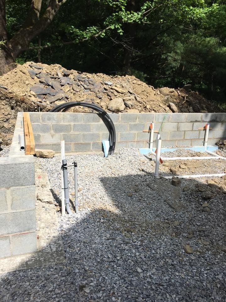 Construction site: cinder block walls, pipes, and gravel base. Sunlight, outdoors.