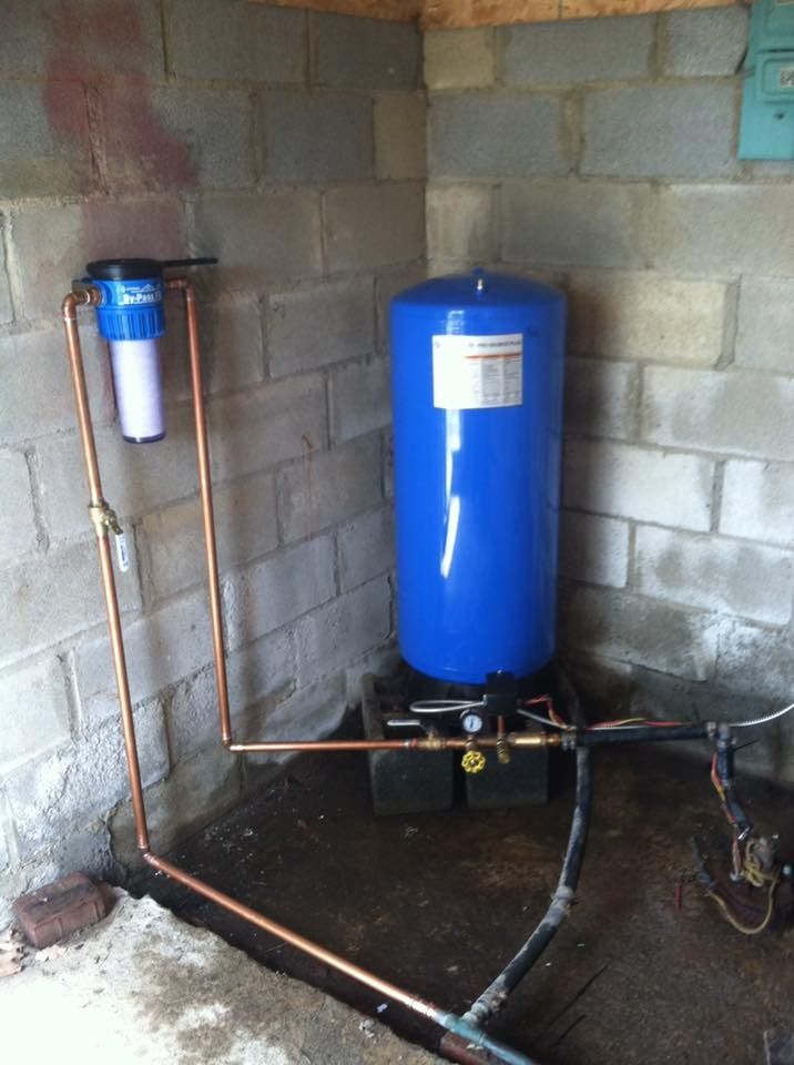Water filtration system with blue tank, copper pipes, and filter in a concrete block room.