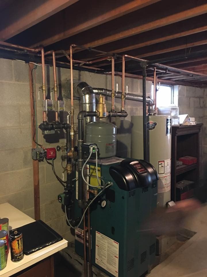 Copper pipes and boiler in a basement, with a green furnace and water heater.