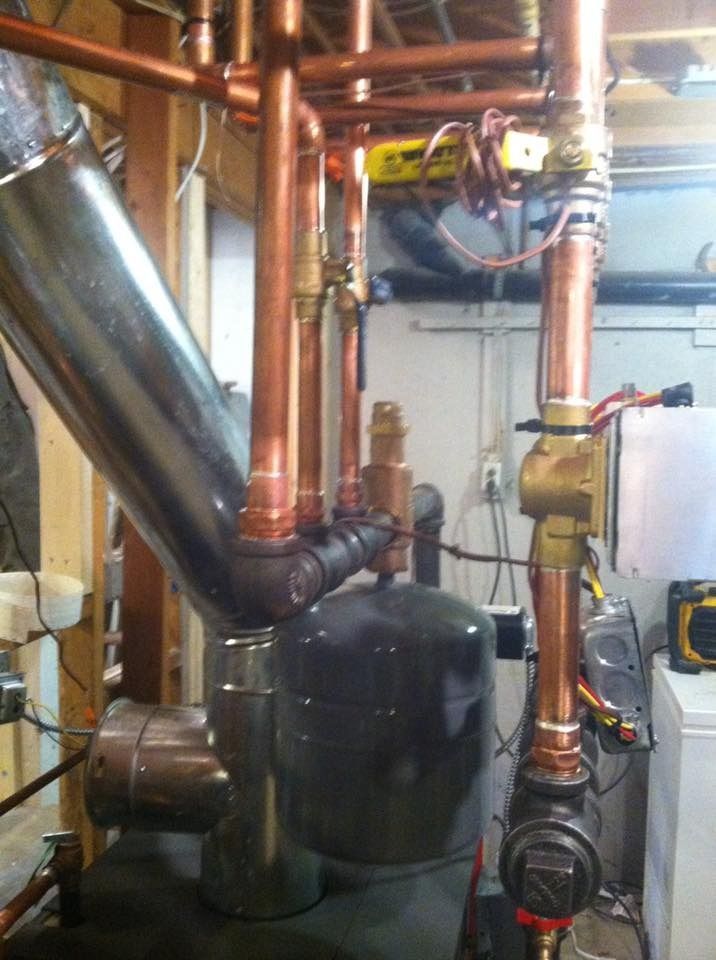 Copper pipes and valves connected to a black tank and mechanical equipment in a basement.