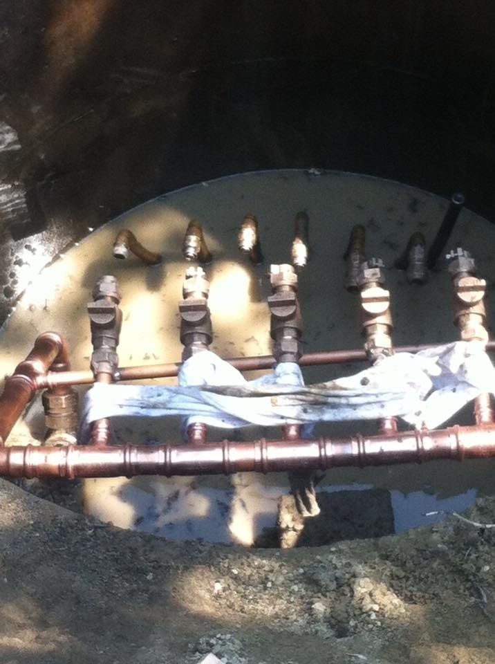 Copper pipes and valves inside a hole in the ground filled with water.