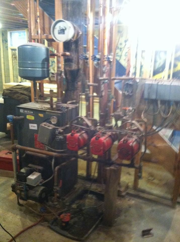 Basement boiler system with copper pipes, red pumps, and expansion tank.