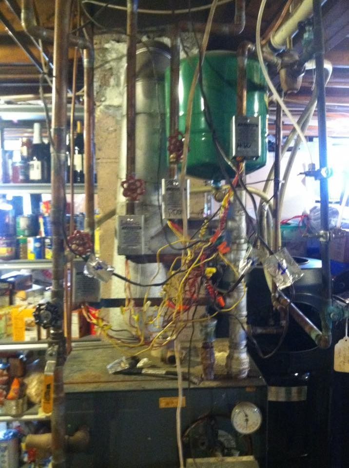A boiler system with copper pipes, green tanks, valves, and exposed wiring in a basement setting.